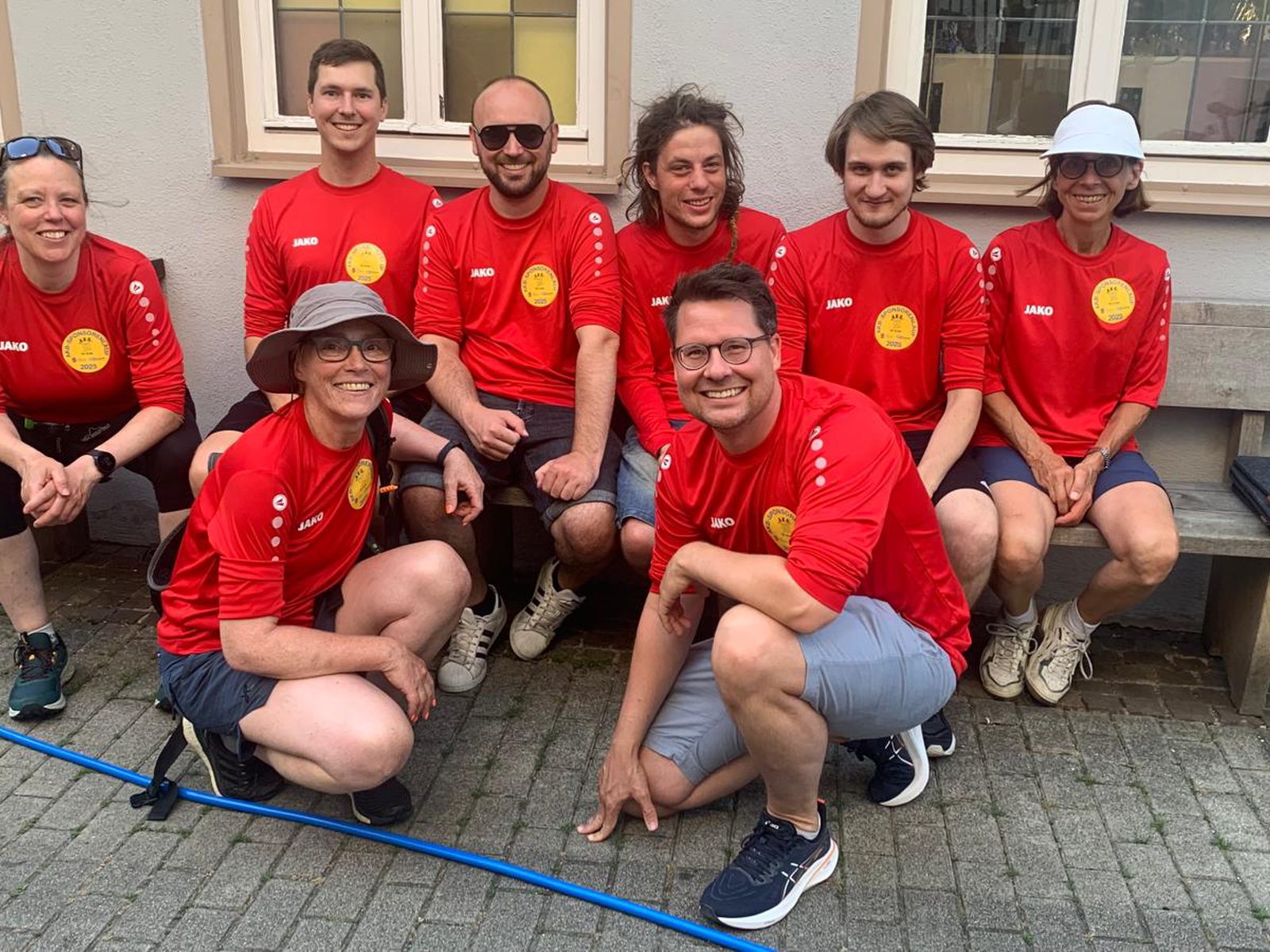 Das Team in roten Sportshirts vor dem Lauf auf und vor einer Holzbank