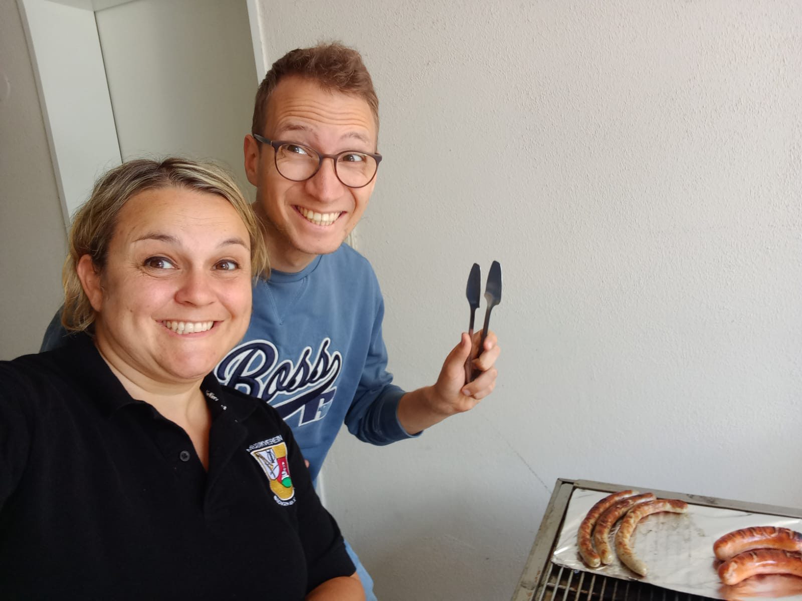 Zwei gut gelaunte Grillende, einer hält die Grillzange in die Höhe