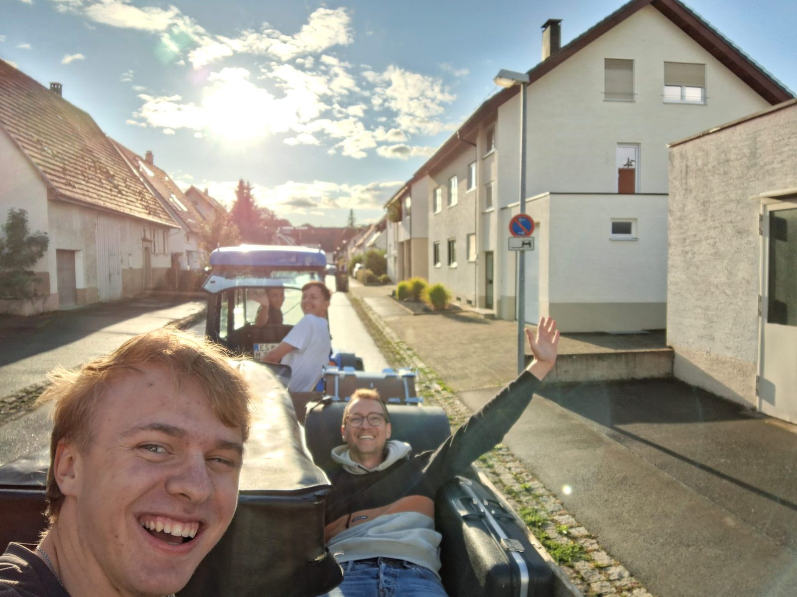 Selfie vor einem Traktor mit Anhänger voller Material, auf dem zwei aus der Aufbau-Crew winken