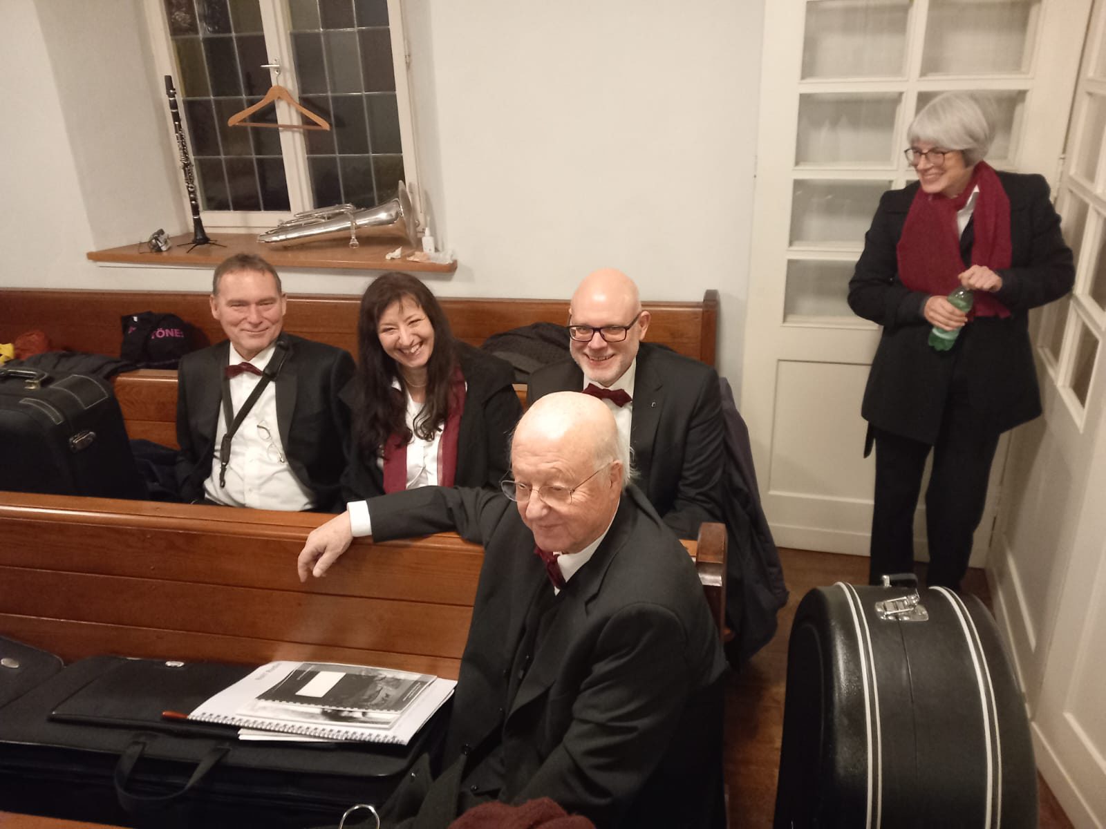 Musiker in Fliege und Schal sitzen in der Kirchenbank, Instrumente auf dem Fenstersims