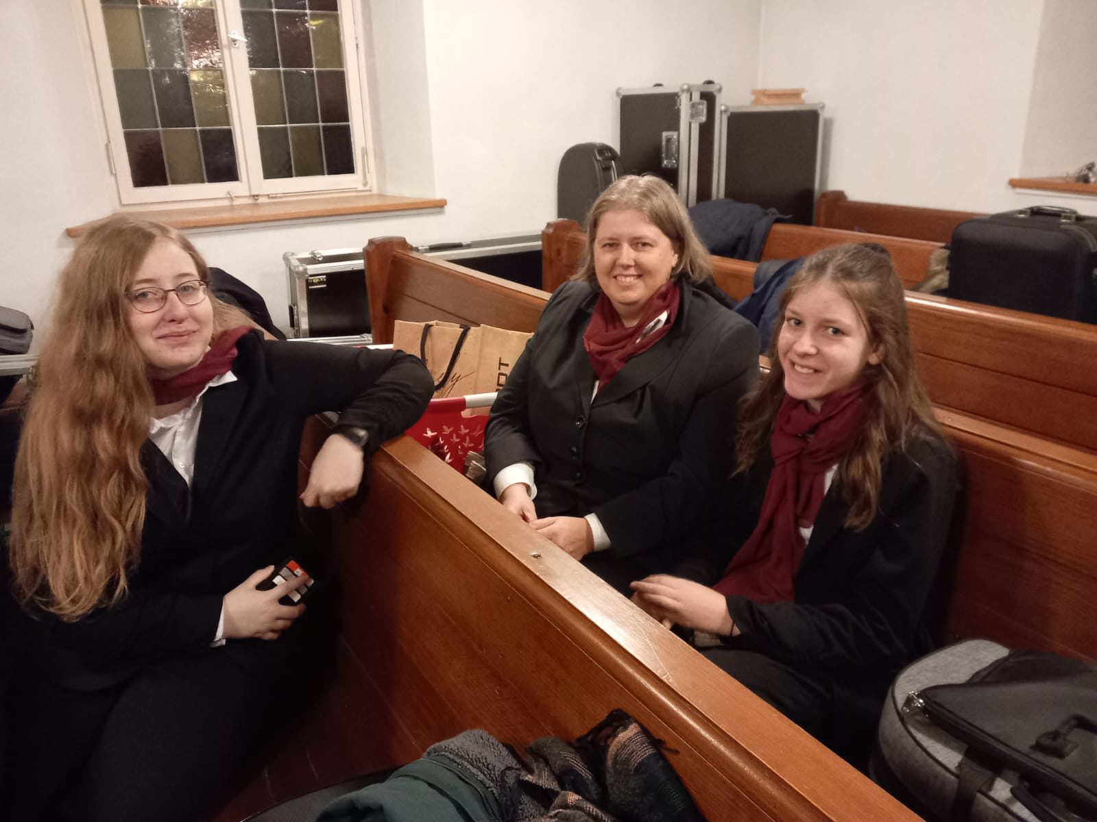 Drei junge Musikerinnen in schwarzen Blazern mit weinroten Schals in der Kirchenbank