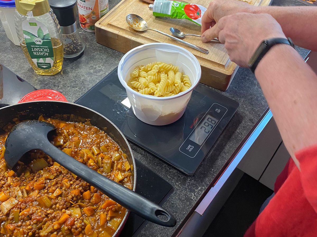 Die fertige Linsenbolognese in der Pfanne, daneben eine Portion Nudeln auf der Küchenwaage
