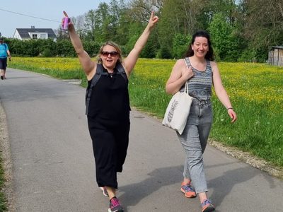 Zwei Wanderinnen auf einem Feldweg durch eine Butterblumenwiese