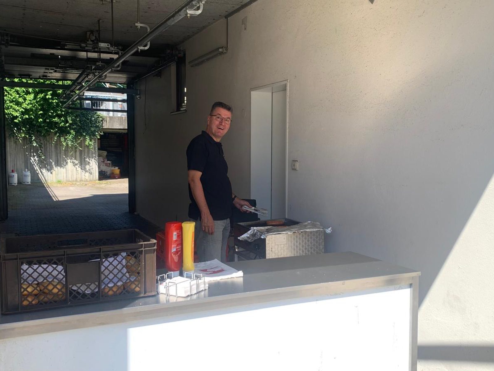 Der Grillstand bei der Metzgerei Schäfer in der Sonne, mit Würsten auf dem Grill, Brötchen, Ketchup und Senf